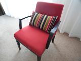 Wooden upholstered armchair with maroon fabric and a colorful striped cushion in front of a window with a net curtain